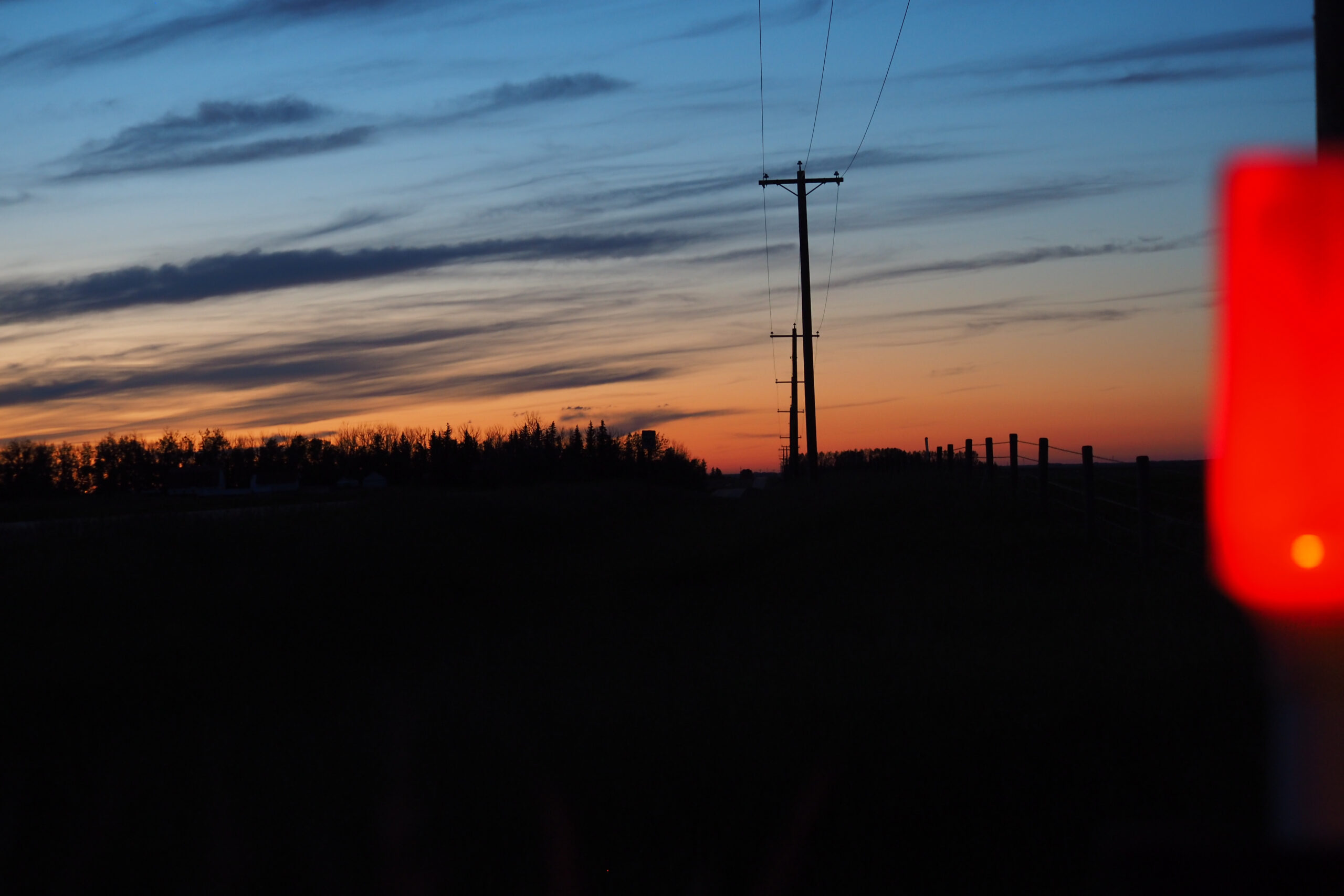 Dusk sky above a dark rural road and power lines, with a blurred red light at the right edge.